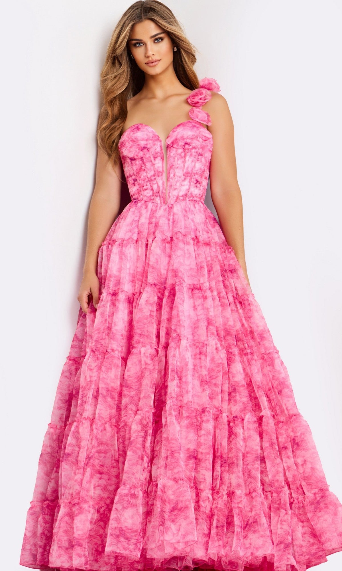 A woman models the Jovani 49074 long prom dress, featuring a bright pink hue, floral single-shoulder strap, and floor-length ruffle details, standing against a plain background.